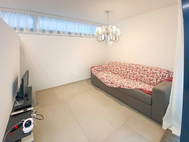 Living room: tile floor, couch, television, chandelier, shelf with remote controls, cables
