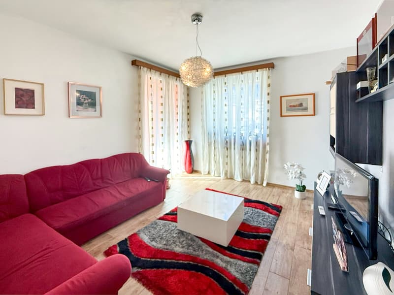 Red sofa, white curtains, framed artwork, wooden floors, coffee table, TV stand