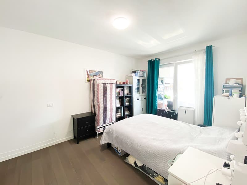 Bedroom with bed, wooden floor, white walls, wardrobe, bed side tables, shelf, window with curtains, air purifier, picture frame on the wall.
