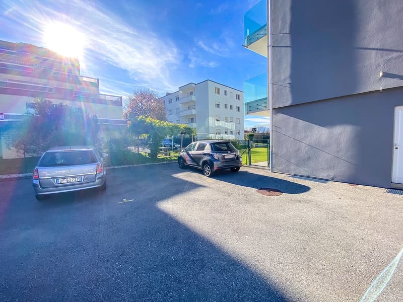 parking lot with two cars parked, gray concrete lot, residential buildings in the background, sunny day