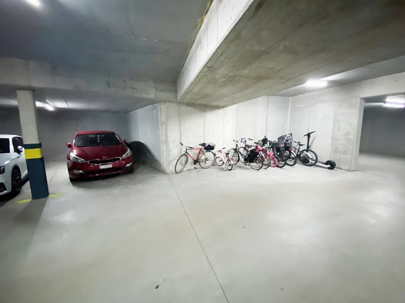 Multiple bicycles, red car, grey parking ceiling