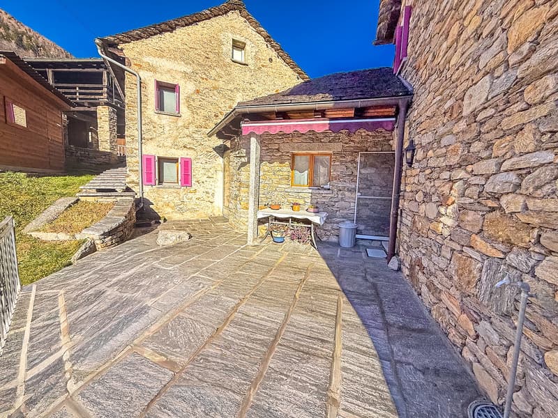 Old stone house with purple shutters, slate roof, pathway, exterior table, outdoor plants