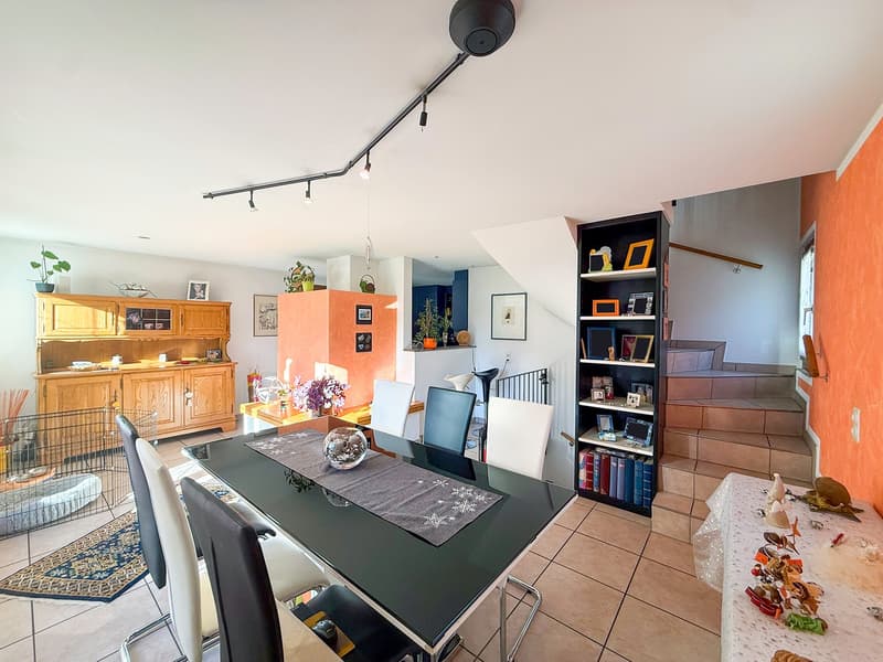 Dining room with wooden cabinet, dining table with chairs, shelves, orange wall, staircase