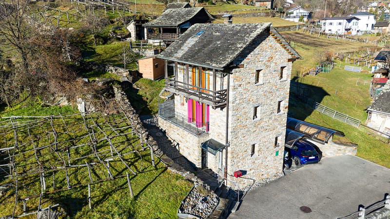 Stone house, 3 levels, balcony, driveway, car parked in garage, surrounded by green landscape