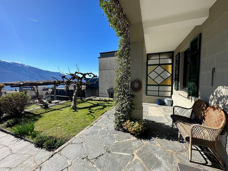 outdoor seating, greenery, paved walkway, a grassy lawn, and a decorative door with colored glass