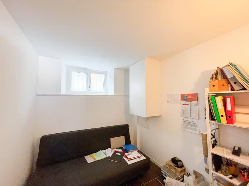 small room, black couch, desk, shelves, white walls, window