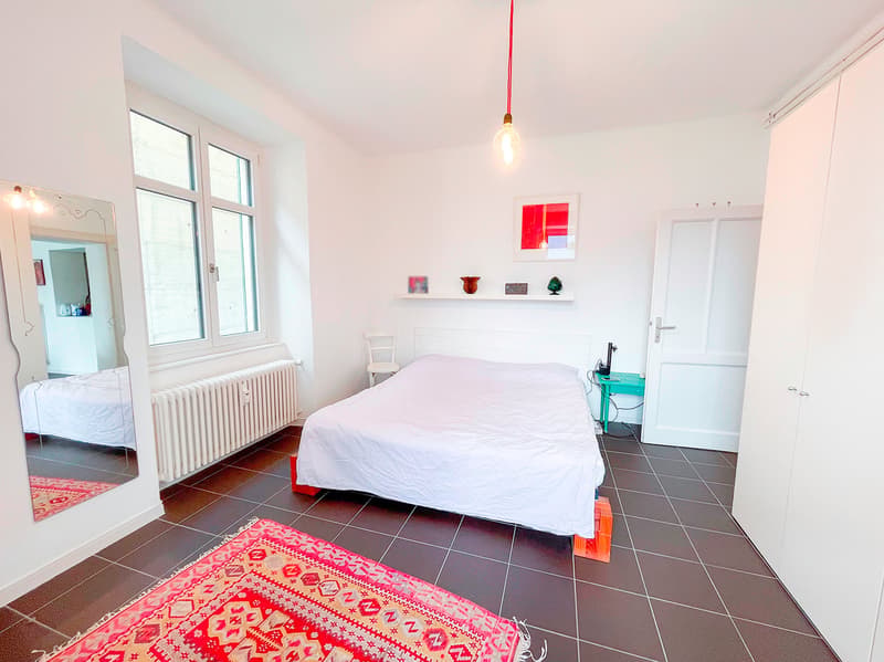 spacious bedroom with a single bed, large window, radiator, rug, mirror, wooden stool