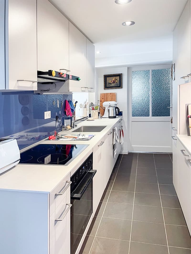 modern kitchen with white cabinets, blue accent wall, tiled flooring, induction stove, dishwasher, toaster, kitchen tools