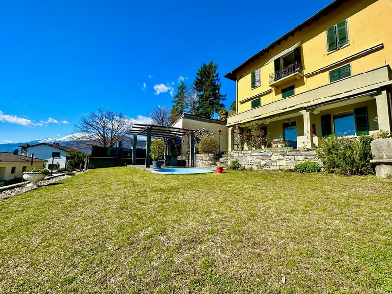 large lawn, swimming pool, stone wall, plants, yellow house, mountains in the background