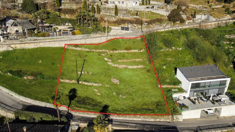 Large flat plot of land on a hill, with a driveway and parking area, with a modern home in the lower right.