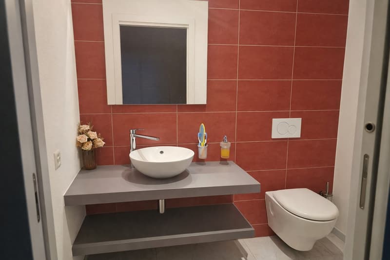 A bathroom with red tiles, a sink with a faucet, a toilet, and a mirror.