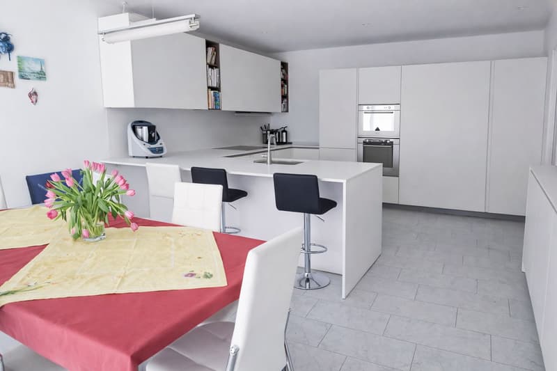 Modern kitchen with white cupboards, kitchen island with bar stools, integrated appliances, central lighting
