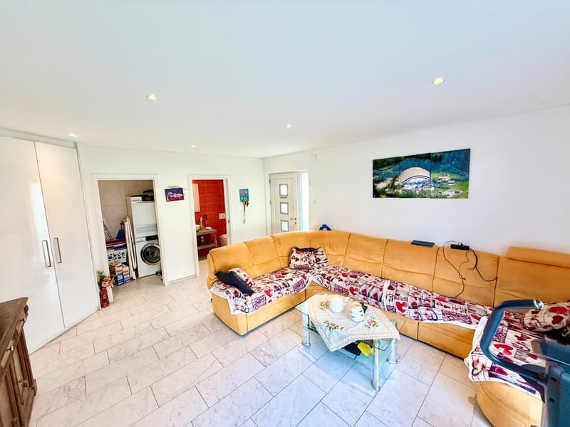 white tile floor, large L-shaped sofa, glass coffee table, white cabinet, washing machine, painting on the wall