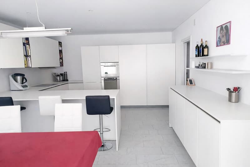 modern kitchen with white cabinets, tile flooring, open bar with chairs, integrated appliances, open shelving, dining table
