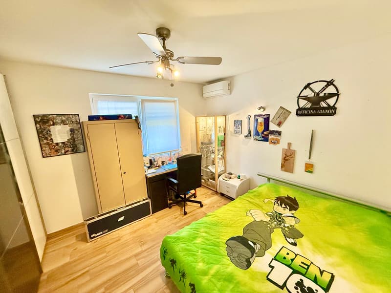 Bedroom with wooden floor, bed, desk, chair, wardrobe, air conditioner, wall decorations, ceiling fan with lights.