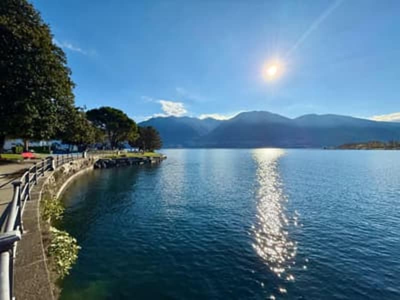 lake surrounded by mountains, clear blue sky, setting sun, pathway along the shore