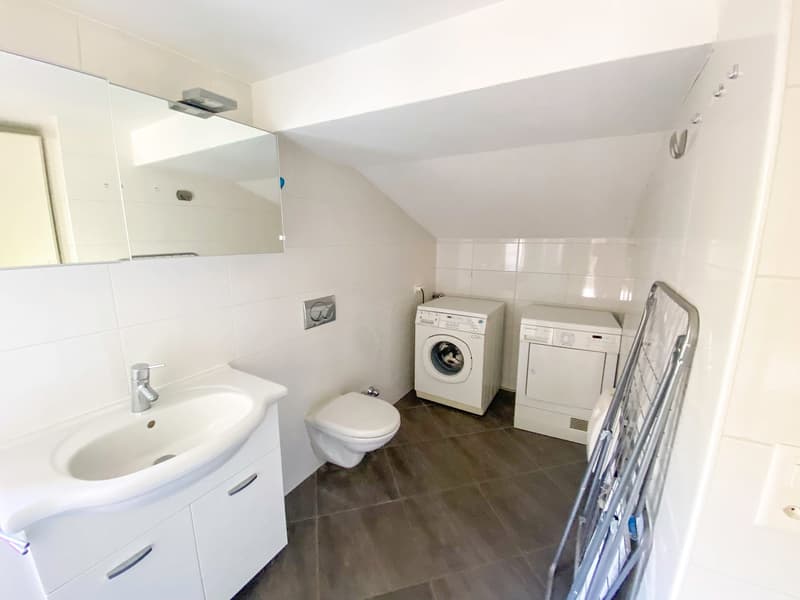 Small bathroom with white tile walls, white cabinets, a mirror, a sink, a toilet, a washing machine, and a dryer.