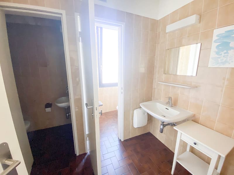tiled walls, tiled floor, white sink, wall-mounted mirror, window, small cabinet