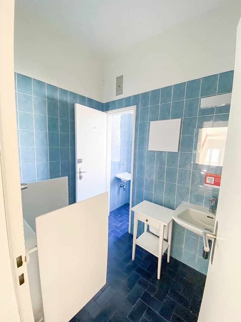 Bathroom with blue tiles, white sink, white doors, white toilet, small shower area, open door, mirror