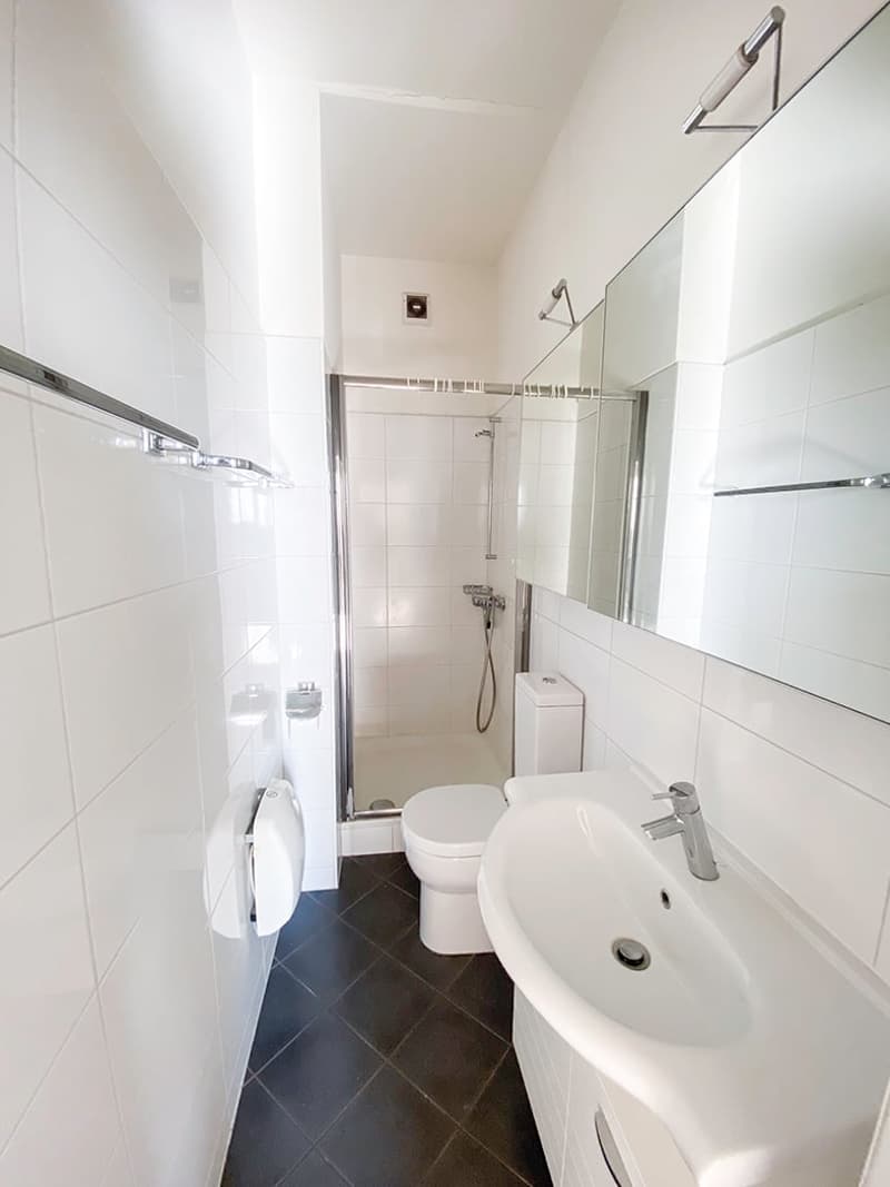 Bathroom with white tiles, a toilet, a shower, and a sink