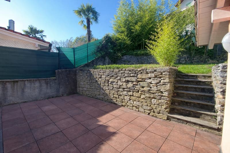 Stone retaining wall, brick paved patio, plants, stone steps, fence, view of trees