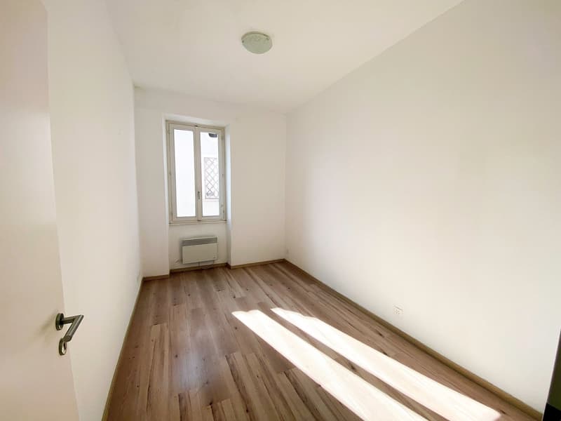 Empty room with wooden floor, white walls, large window, ceiling light, no furniture