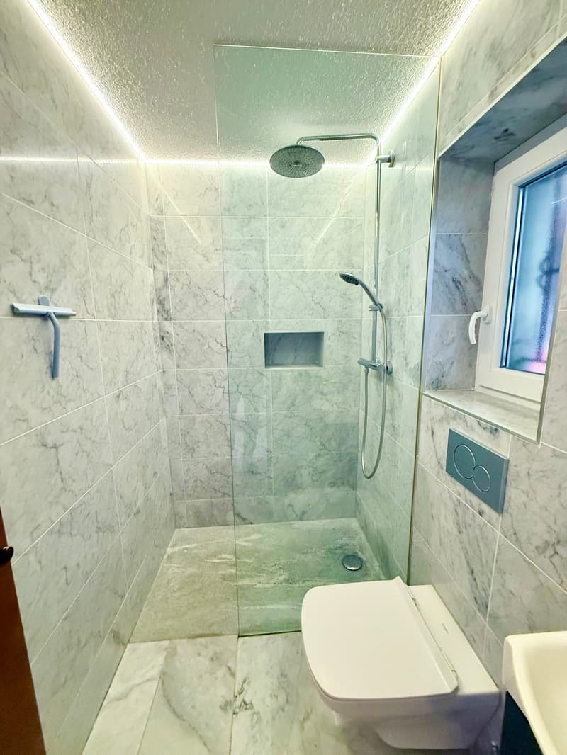 modern and clean, white toilet, shower, large window, white sinks, marble floors and walls