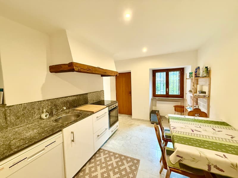 marble countertop, white cabinets, modern appliances, wooden beams, wooden door, radiator, dining table, wooden chairs