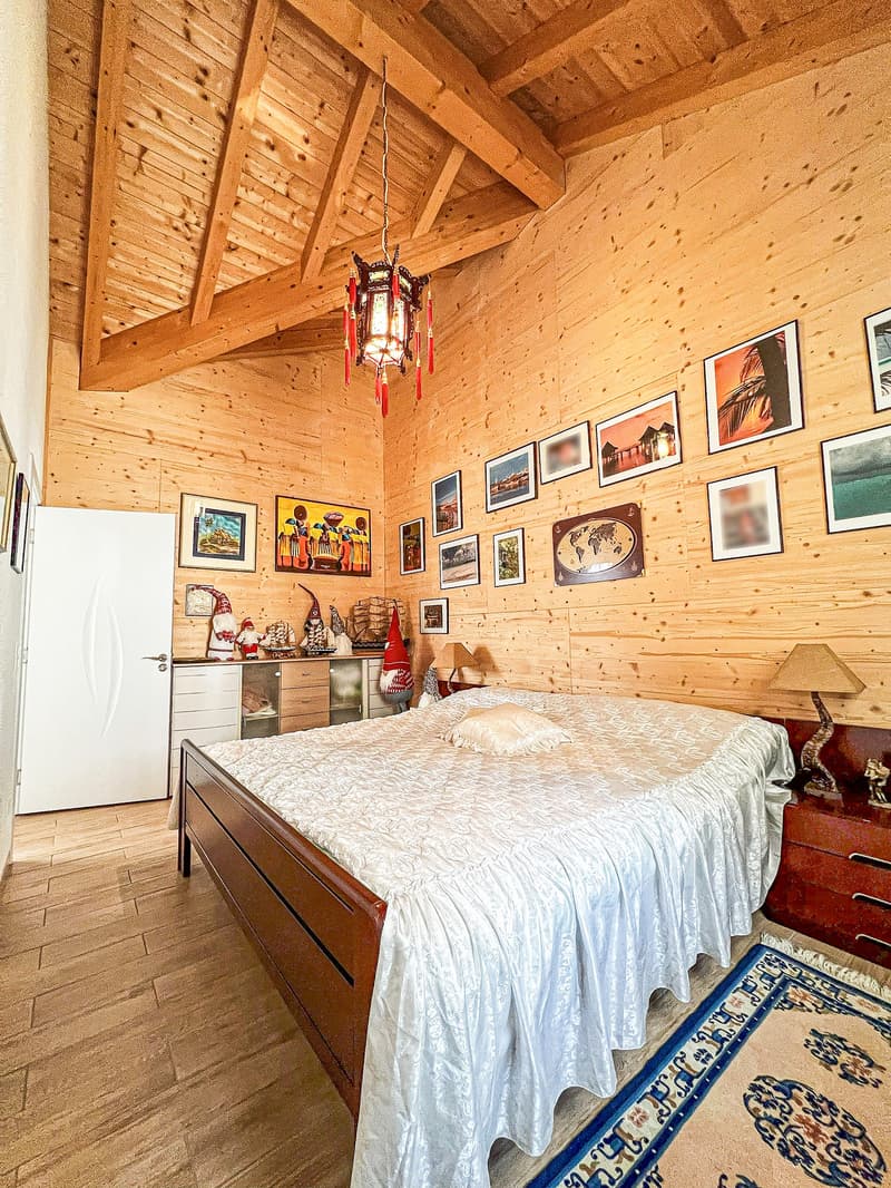 Wooden cabin-style bedroom with exposed wooden beams and walls, a large bed with a patterned comforter, a hanging lantern-style light fixture, and various framed artwork and decorative items on the walls.