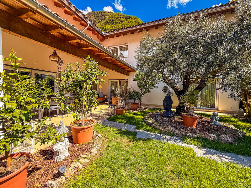 Garden with various potted plants, walking path, wooden pergola, statues, and green grass