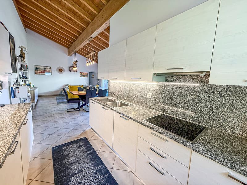 Open kitchen with wooden ceiling beams, white cabinets, granite countertops, tile flooring, and a dishwasher visible