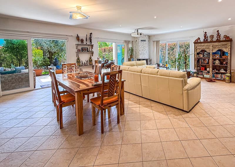 modern dining room with wooden table and chairs, large white couch, sliding doors leading to the garden