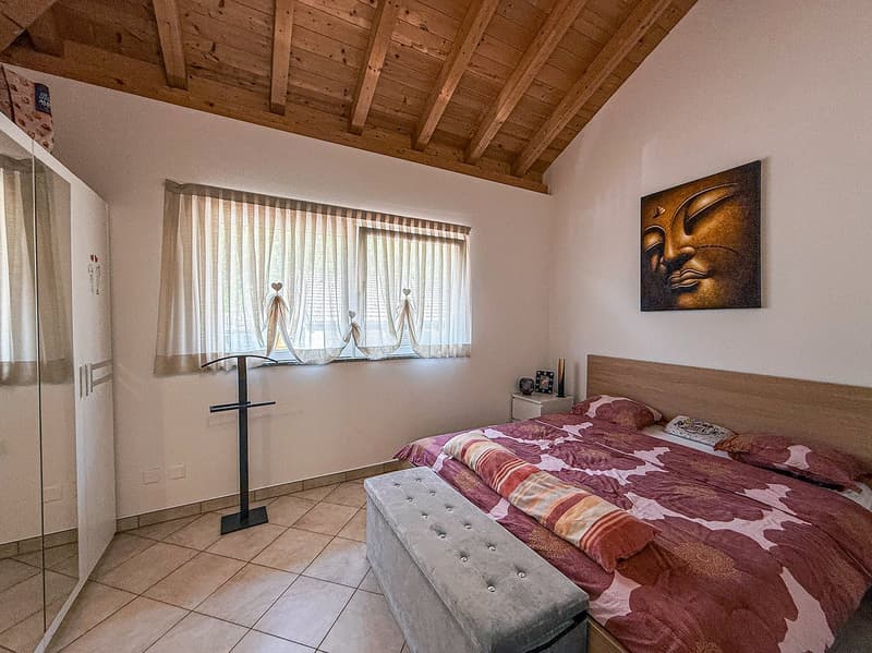 Spacious bedroom with wooden ceiling beams, large windows, a tufted bench at the foot of the bed, and a decorative Buddha artwork on the wall.