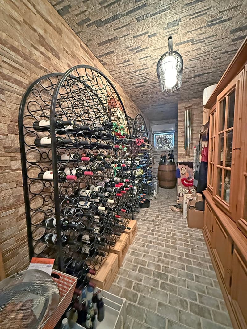Large wine cellar with brick walls and ceiling, extensive wine rack storage, decorative lighting fixture, and additional shelving and storage space