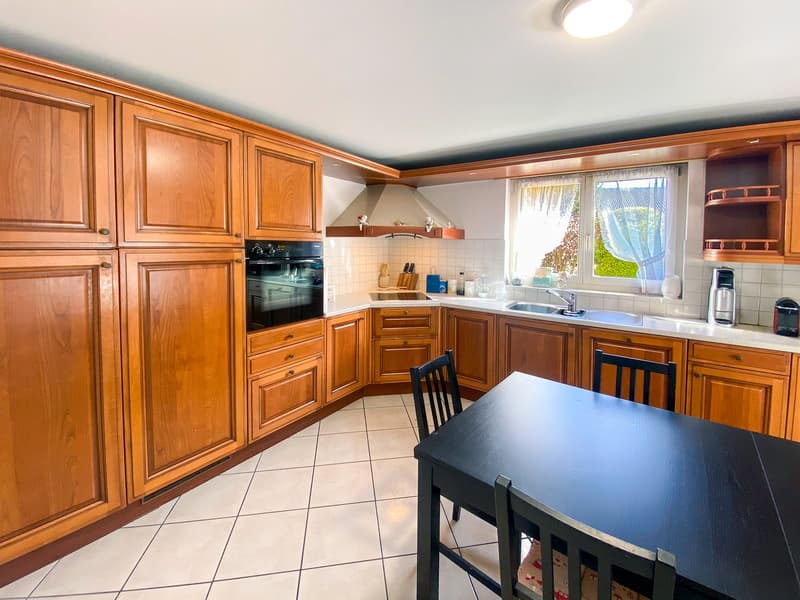 modern kitchen with wooden cabinets, white tiled floor, black dining table, sink, oven, dishwasher, coffee machine