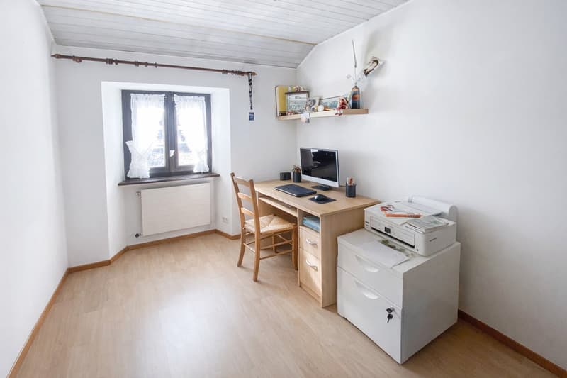 wooden floor, white walls, desk with computer, printer, chair, window with curtains, radiator