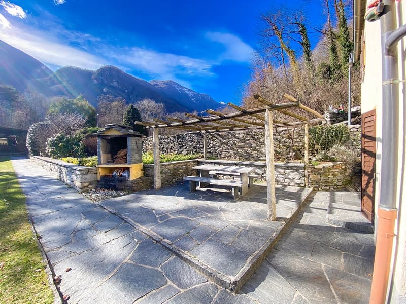 Outdoor stone pergola seating, outdoor fireplace, stone retaining wall, gravel path, green grass, mountains in the distance