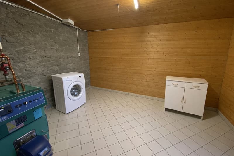 A storage room with white tile flooring, wooden wall, washing machine, wooden cabinet and pipes on the wall