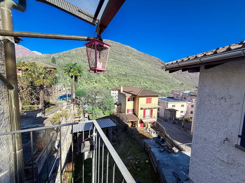 The image shows a residential area with colorful buildings, palm trees, and a mountainous backdrop. There is a red lantern-style light fixture visible on the balcony or terrace of one of the buildings.