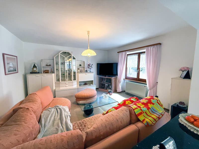 Spacious living room with large windows, pink and orange sofa, glass coffee table, TV stand, display cabinet, and colorful decorative pillows