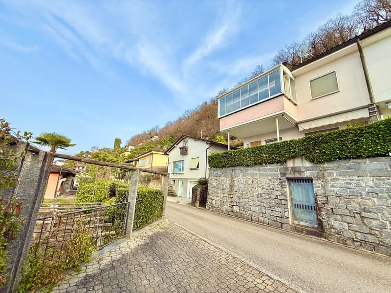 Houses on a cobblestone street, stone walls, hedges, and a hillside in the background.