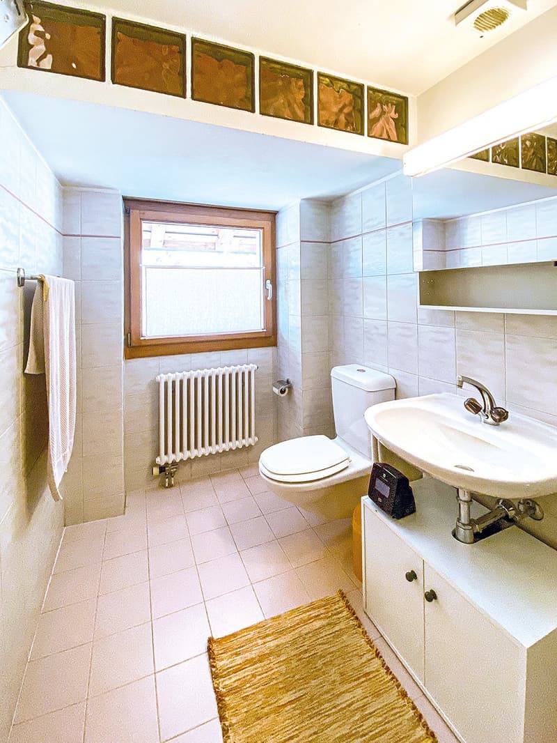 Bathroom with white tiles, white toilet, white sink, white radiator, small window, towel rack, and a rug