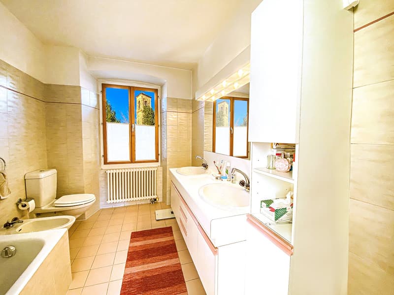 Bathroom with bathtub, double sink, toilet, bidet, radiator, window, tiled floor, rug