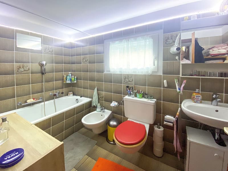 Bathroom with bathtub, bidet, toilet, sink, shelves, and tiled walls