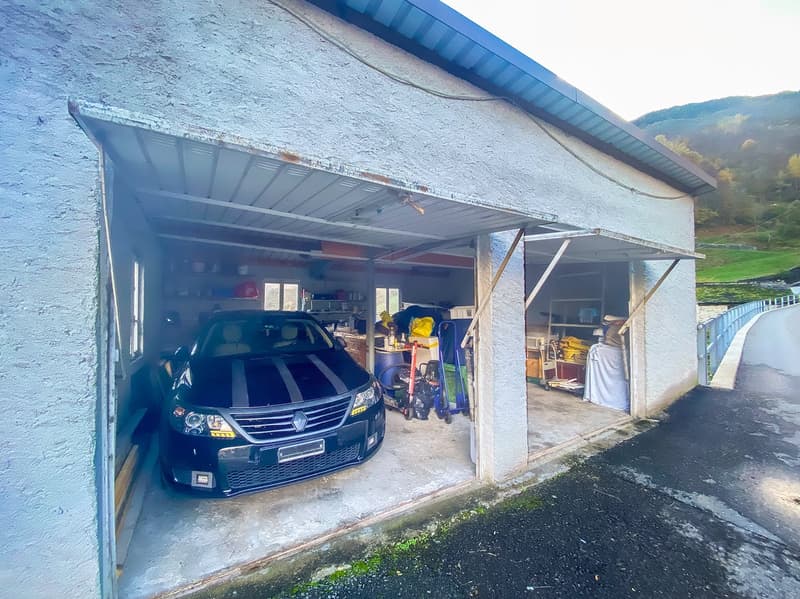 A car parked in a garage with shelves, storage boxes, and a trolley