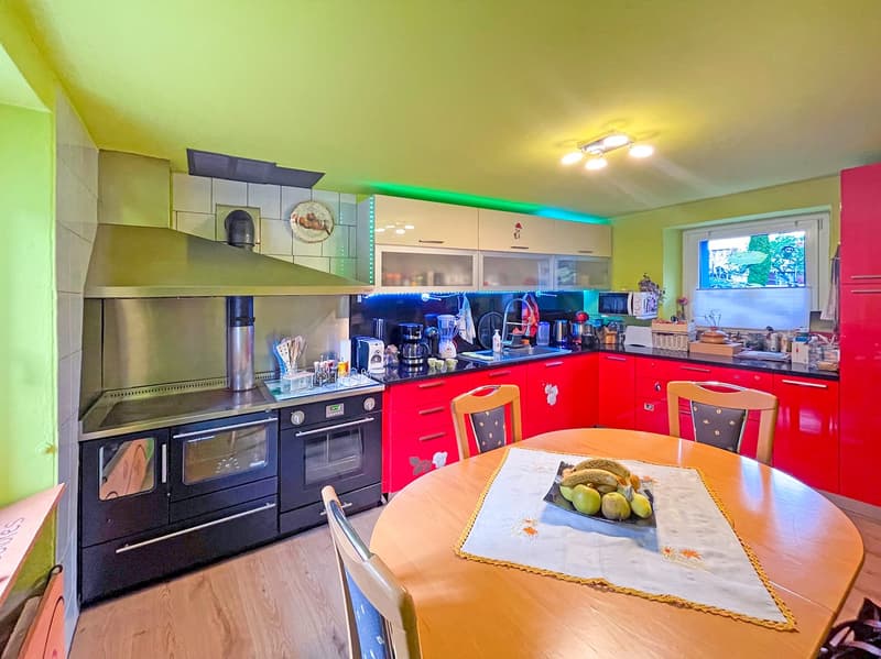 modern kitchen with red cabinets, yellow walls, wooden table, chairs, oven, microwave, refrigerator, sink, countertop, fruit on table
