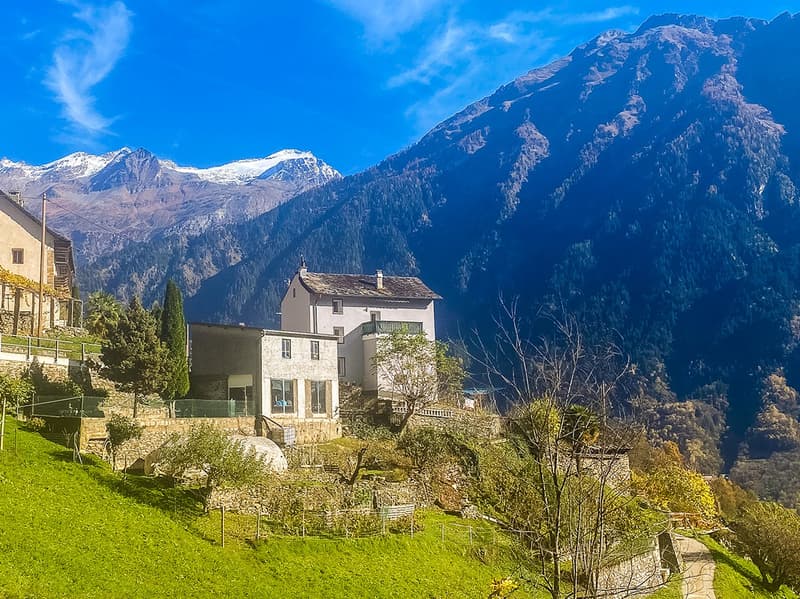 House on a hill, surrounded by mountains, with a garden and a pathway