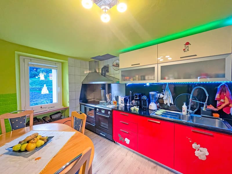 kitchen with dining area, wooden table, chairs, red and white cabinets, green walls, window, appliances, fruits on table