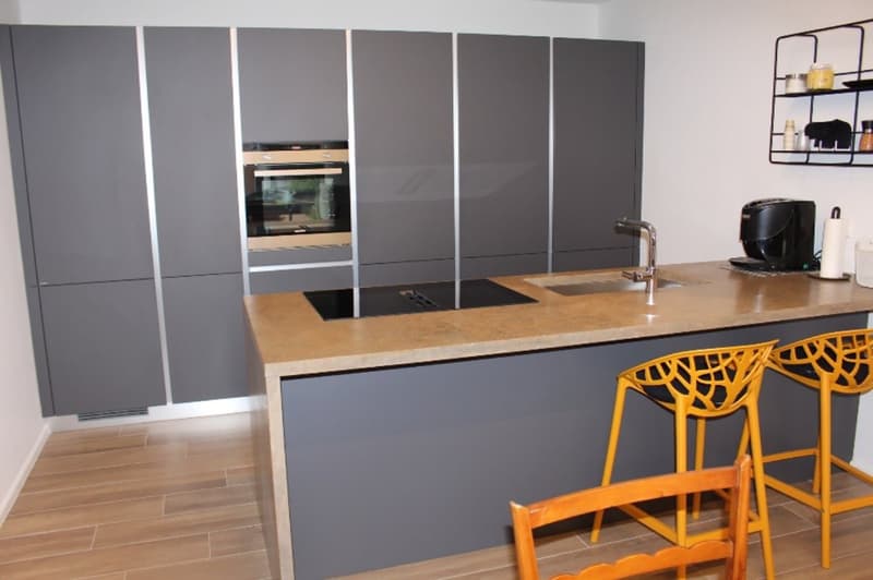 modern kitchen with gray cabinets, wooden floor, island with sink and stove, coffee machine, yellow chairs