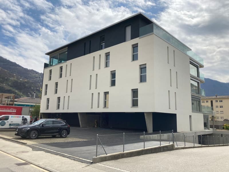 Modern white building with glass windows, black accents, underground garage, located in a mountainous area